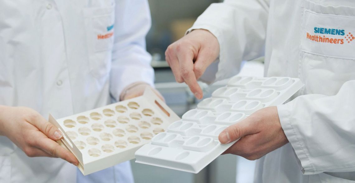 Zwei Personen im Siemens Healthineers Laborkittel halten und vergleichen nachhaltige Verpackungstrays für Laborproben.