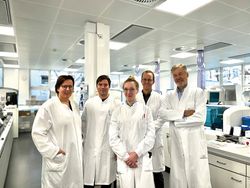 DKLM 2025 - das Leipziger Kongressteam. Fünf Labormitarbeiter:innen im weißen Kittel stehen lächelnd in einem modernen Diagnostiklabor.